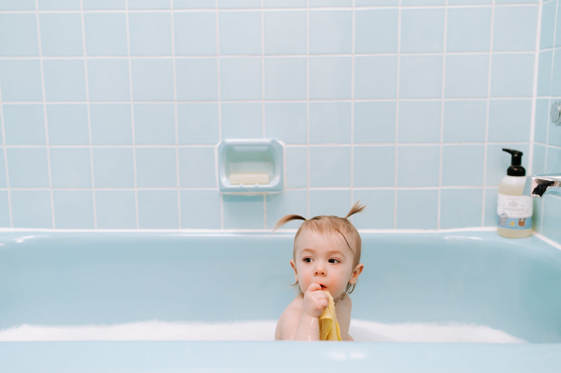 Toddler in the bath holding a yellow washcloth freshly washed with fragrance-free detergent