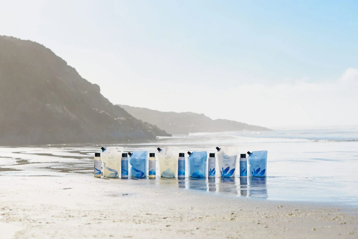 Row of shampoo and conditioner refill pouches lined up on a beach shoreline