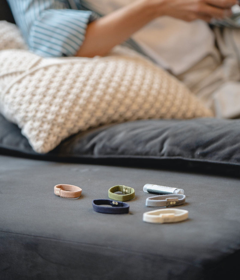 Various colored fabric hair ties and a lip balm on a couch with someone relaxing in the background.