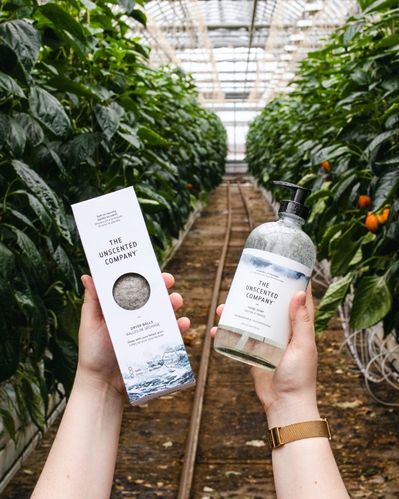 Hands holding The Unscented Company dryer balls and hand soap in a greenhouse.