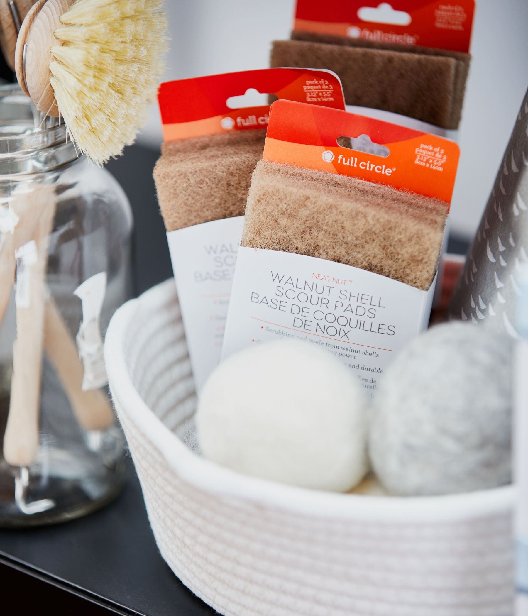 Tampons à récurer en coquille de noix dans un panier avec des balles de séchage en laine et des brosses.