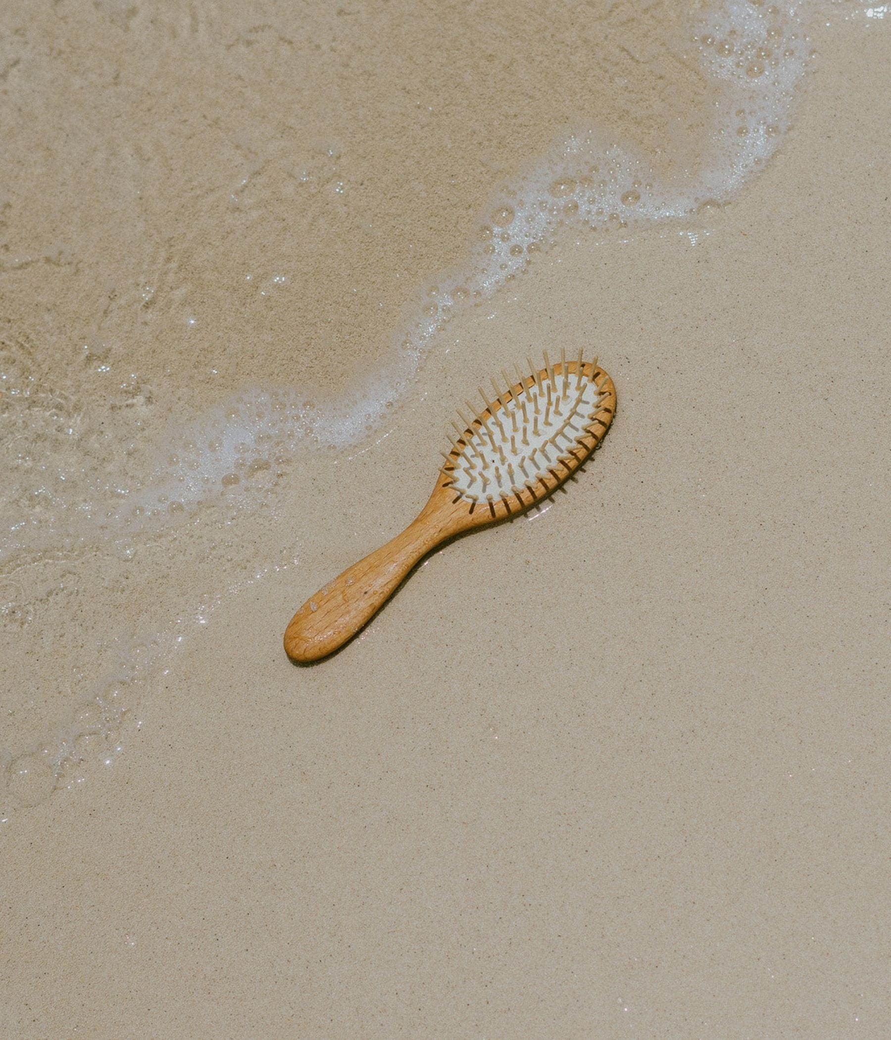 Wooden hairbrush lying on wet sand near the shoreline.
