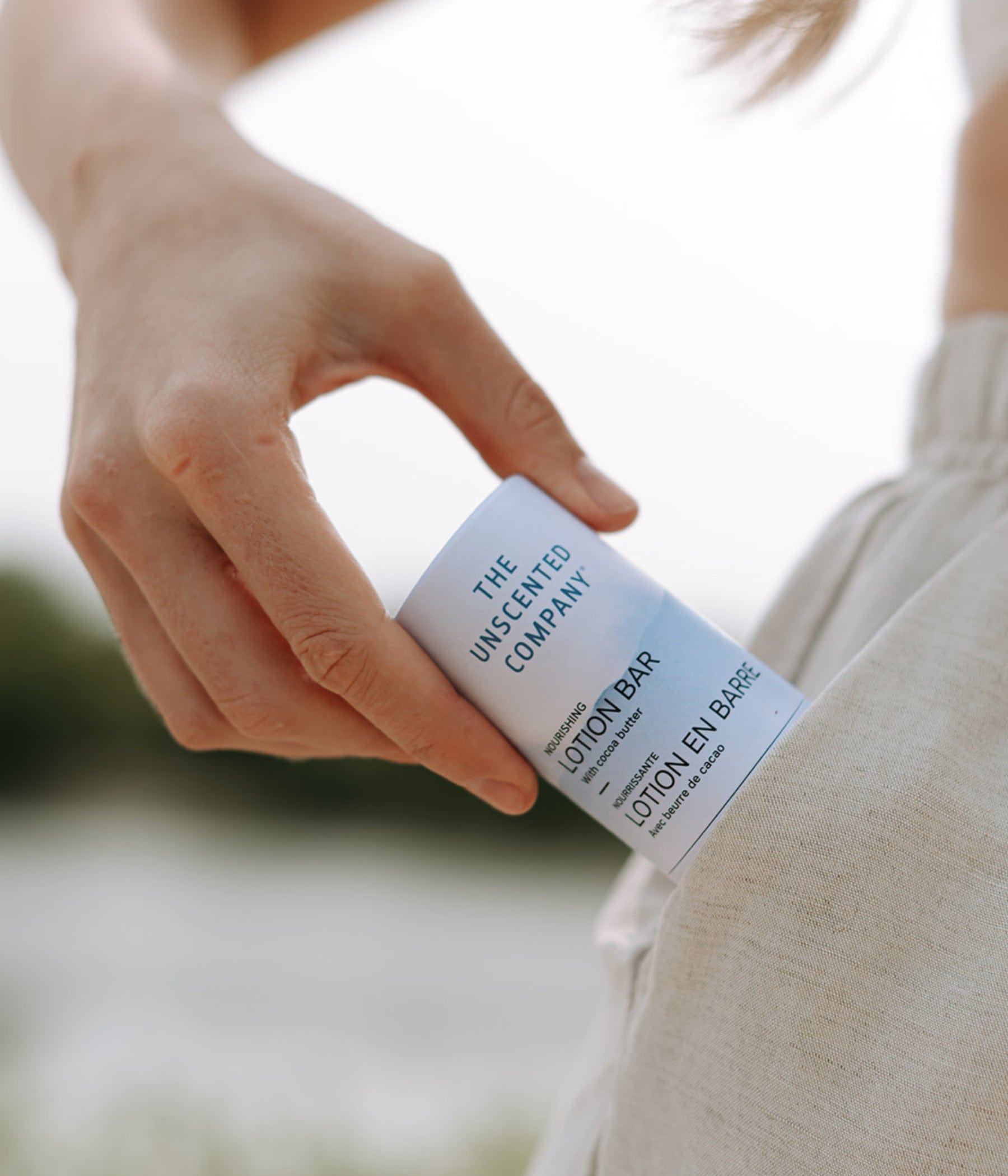 Close-up of a hand slipping The Unscented Company’s lotion bar into a linen pocket outdoors.