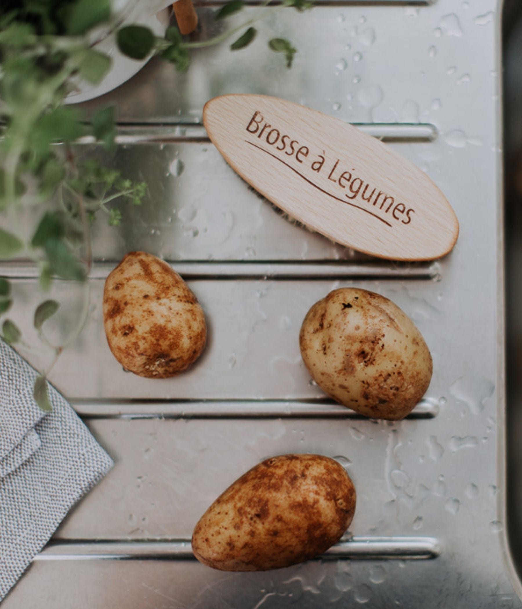Brosse à légumes en bois avec des pommes de terre sur une surface en acier inoxydable mouillée.
