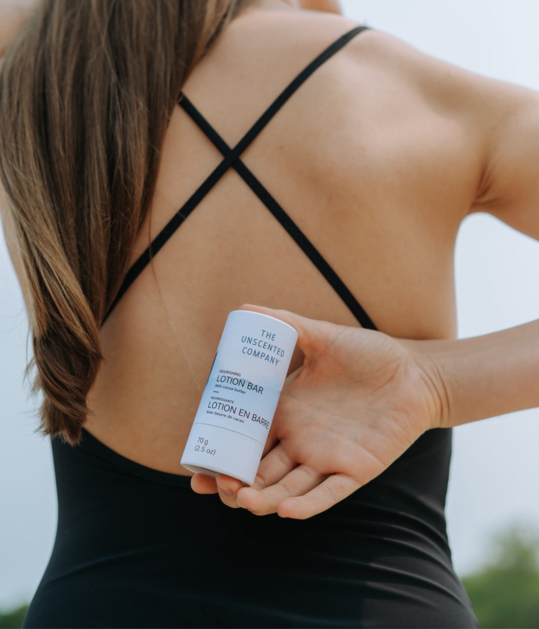 Back view of a person in a black swimsuit holding The Unscented Company’s lotion bar behind their back.
