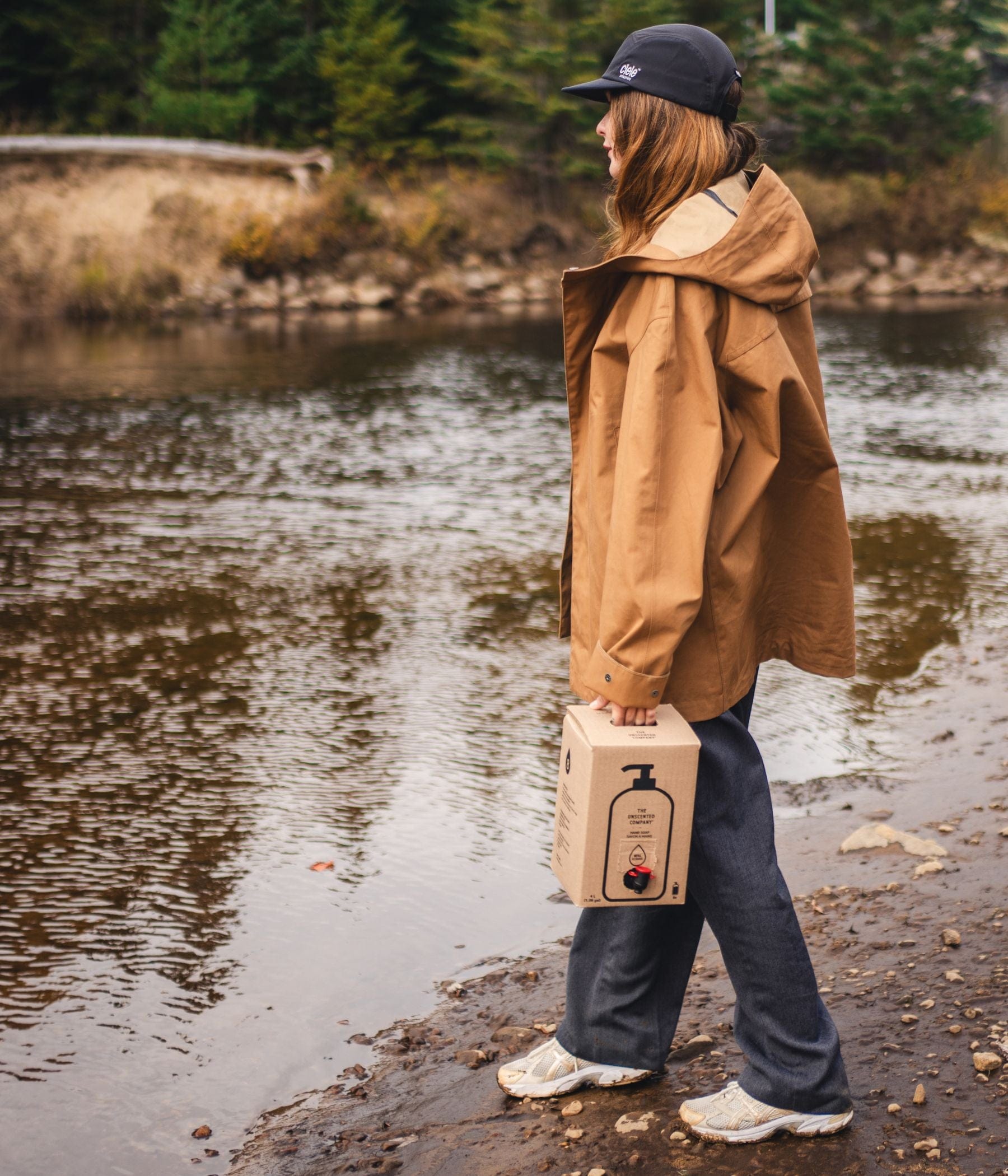 Person standing by the water holding a box of The Unscented Company hand soap.
