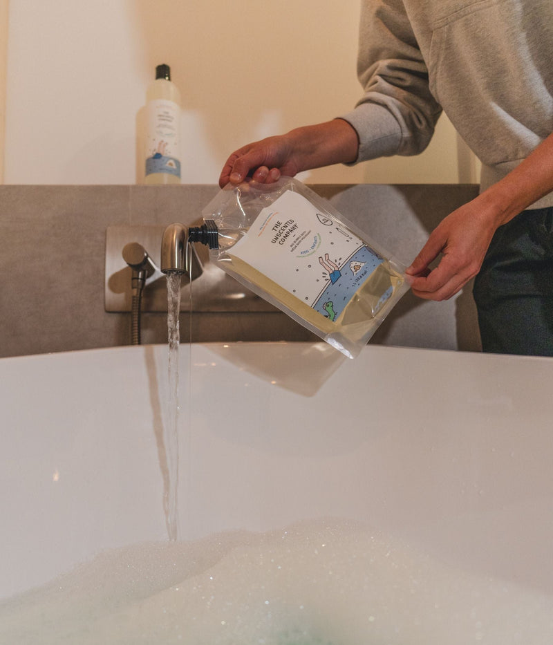 Person pouring The Unscented Company bubble bath into a tub.