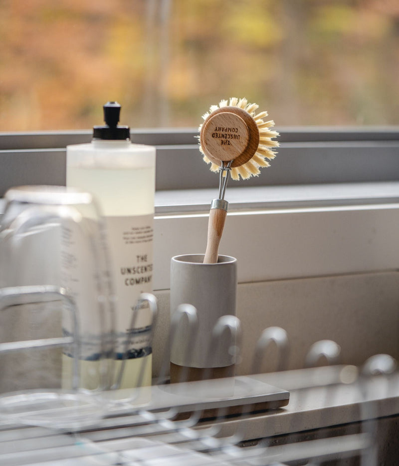 The Unscented Company dish brush and dish soap by a kitchen sink.