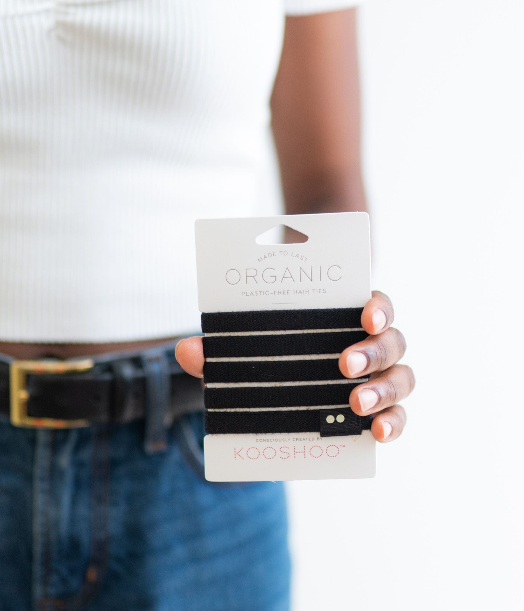 Person holding a pack of black KOOSHOO hair ties.