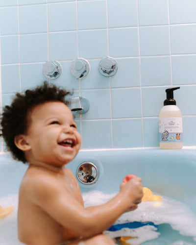 Smiling child playing in a bubble bath with soap bottle nearby
