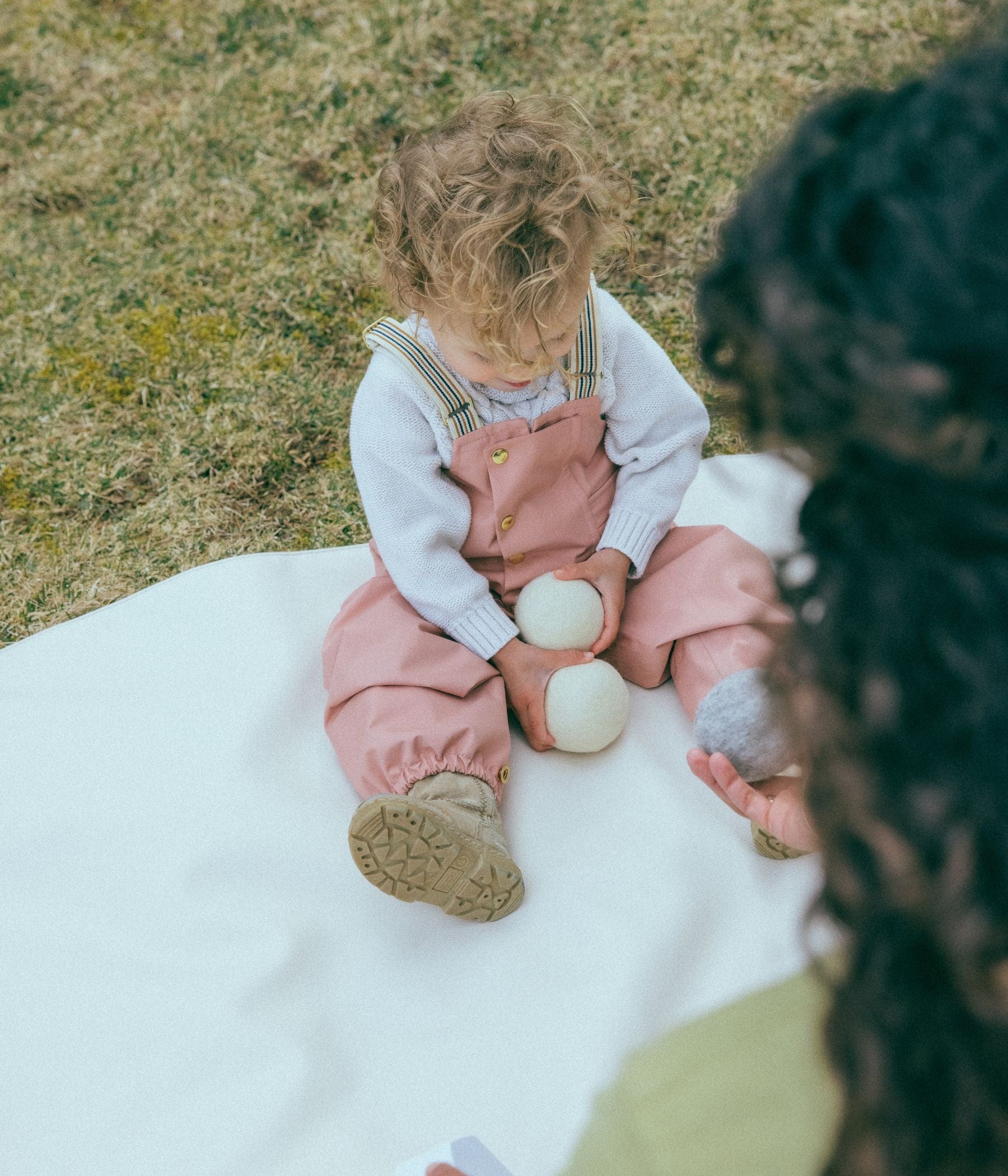 A toddler sitting on a white blanket, holding wool dryer balls.