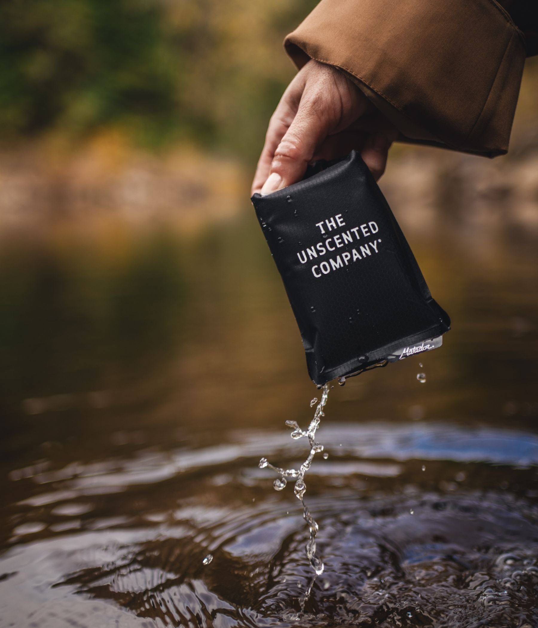 Hand holding a wet The Unscented Company pouch over water.