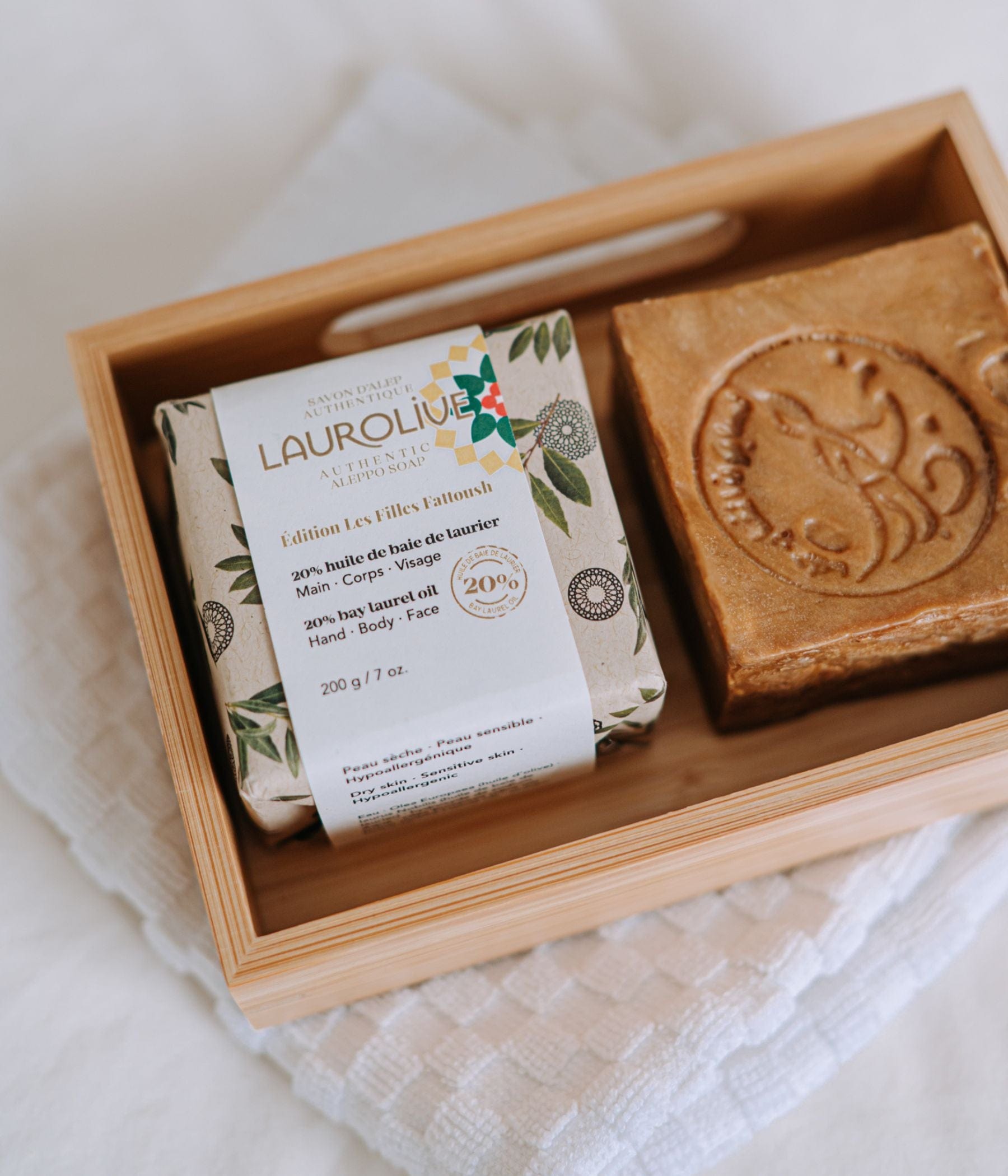 A wrapped and an unwrapped Laurolive soap bar placed in a wooden tray on a white cloth.