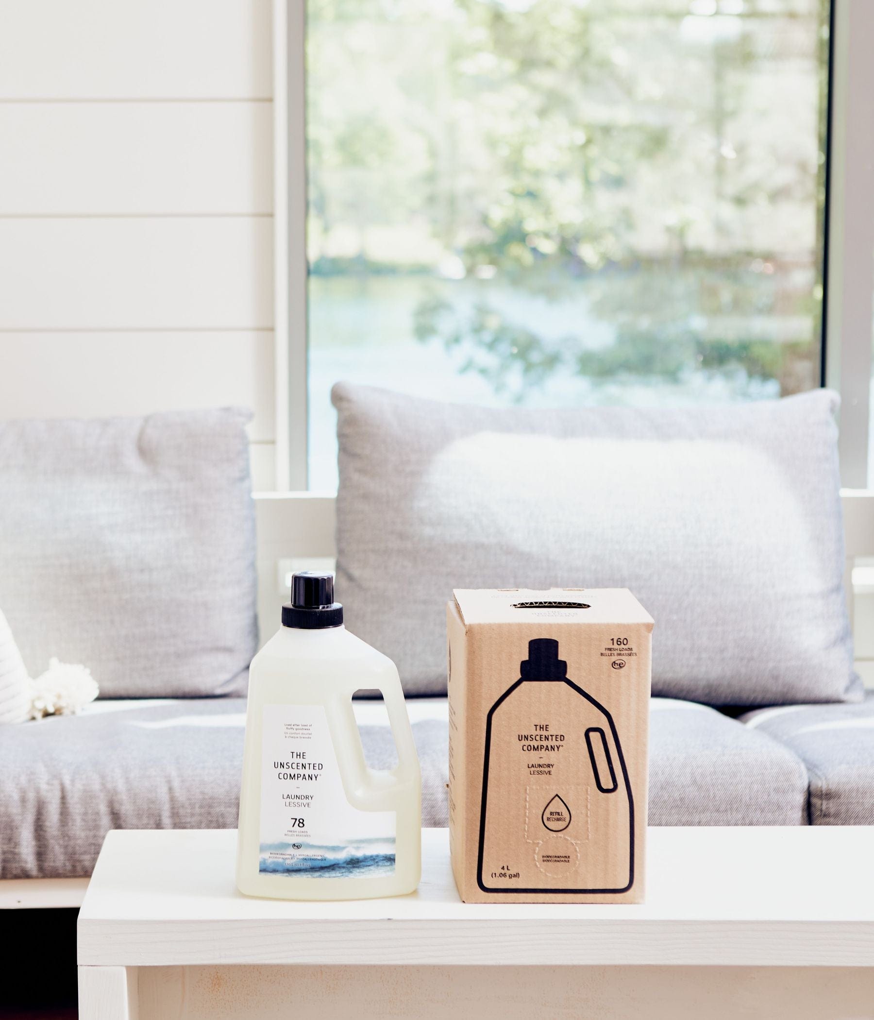 Refillable laundry detergent bottle and box on a white table in front of a sofa.