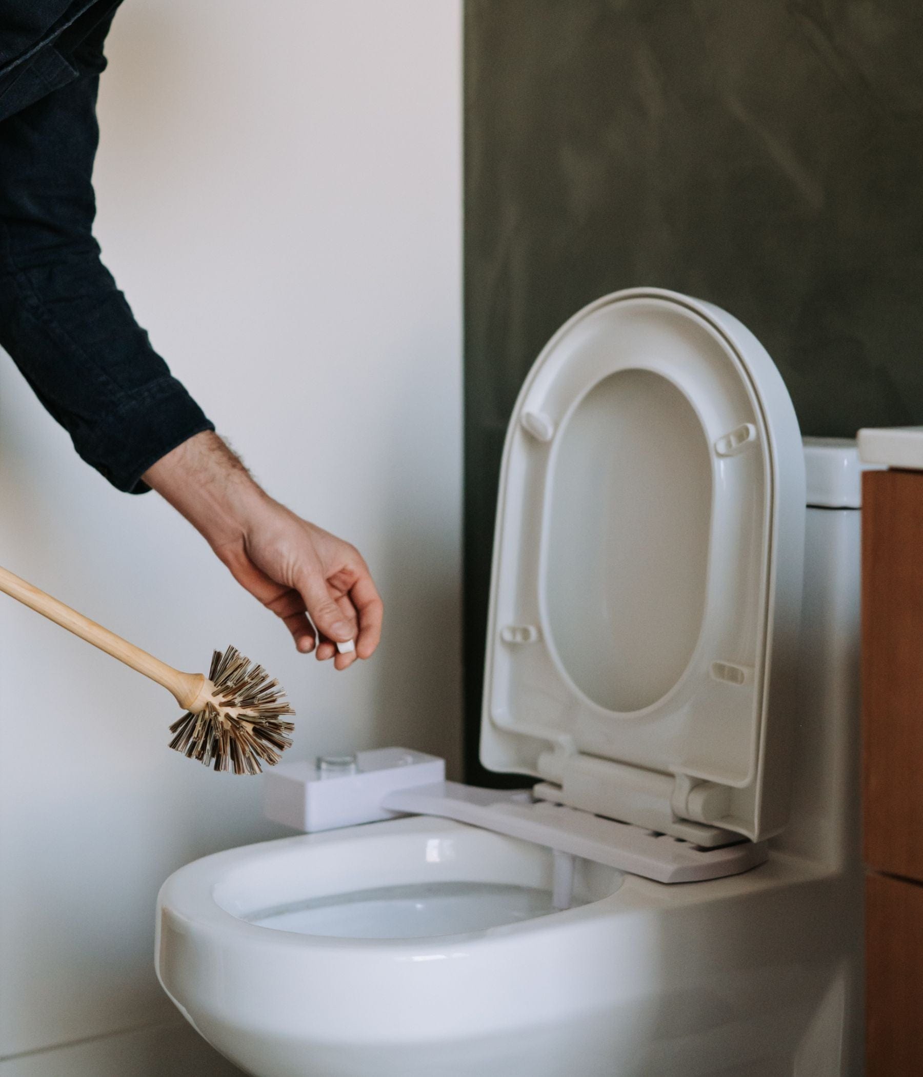 Someone about to drop a tab of Toilet Bowl Cleaner - 22 tabs in a toilet with a toilet brush in their right hand.