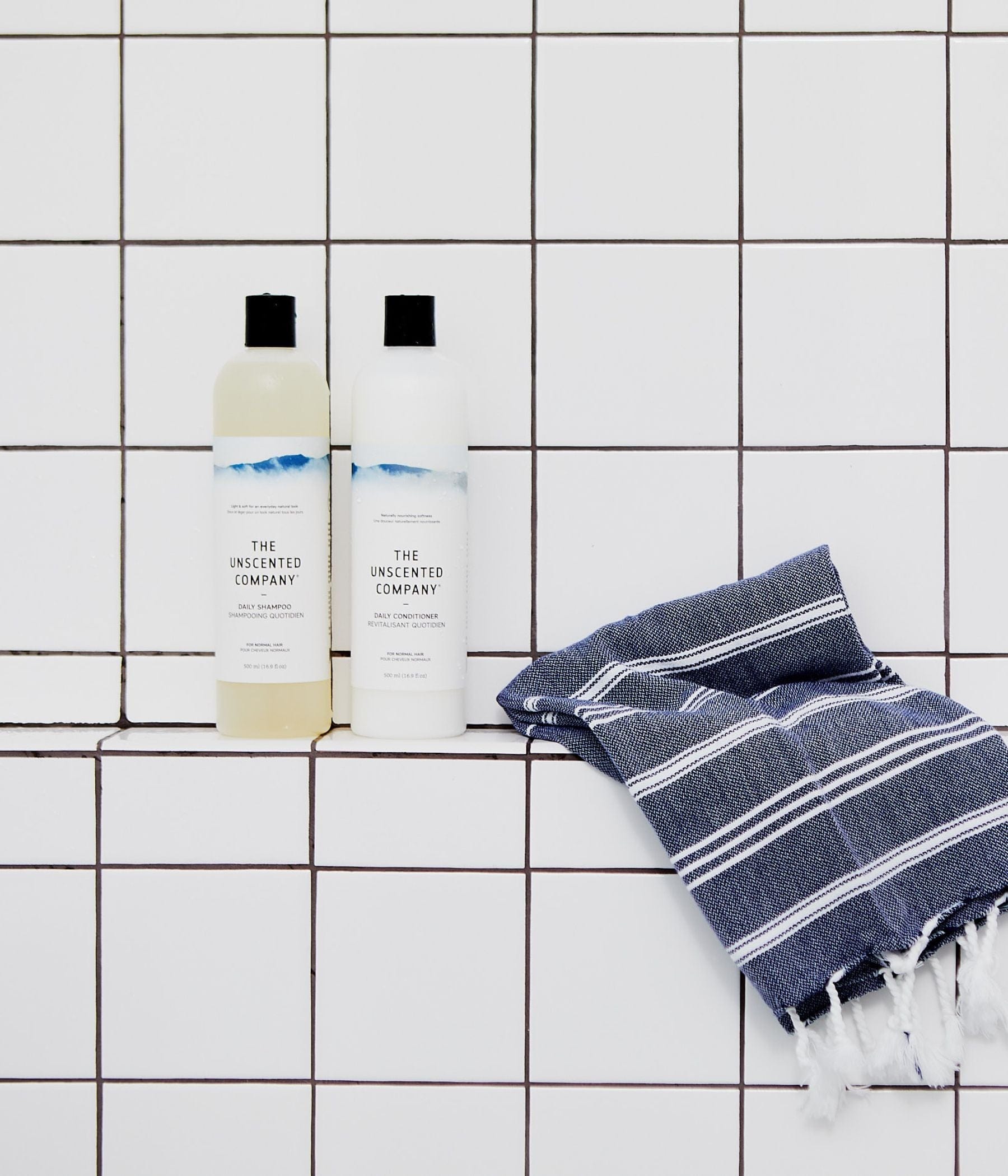 Shampoo and conditioner bottles from The Unscented Company with a towel on a tiled surface.
