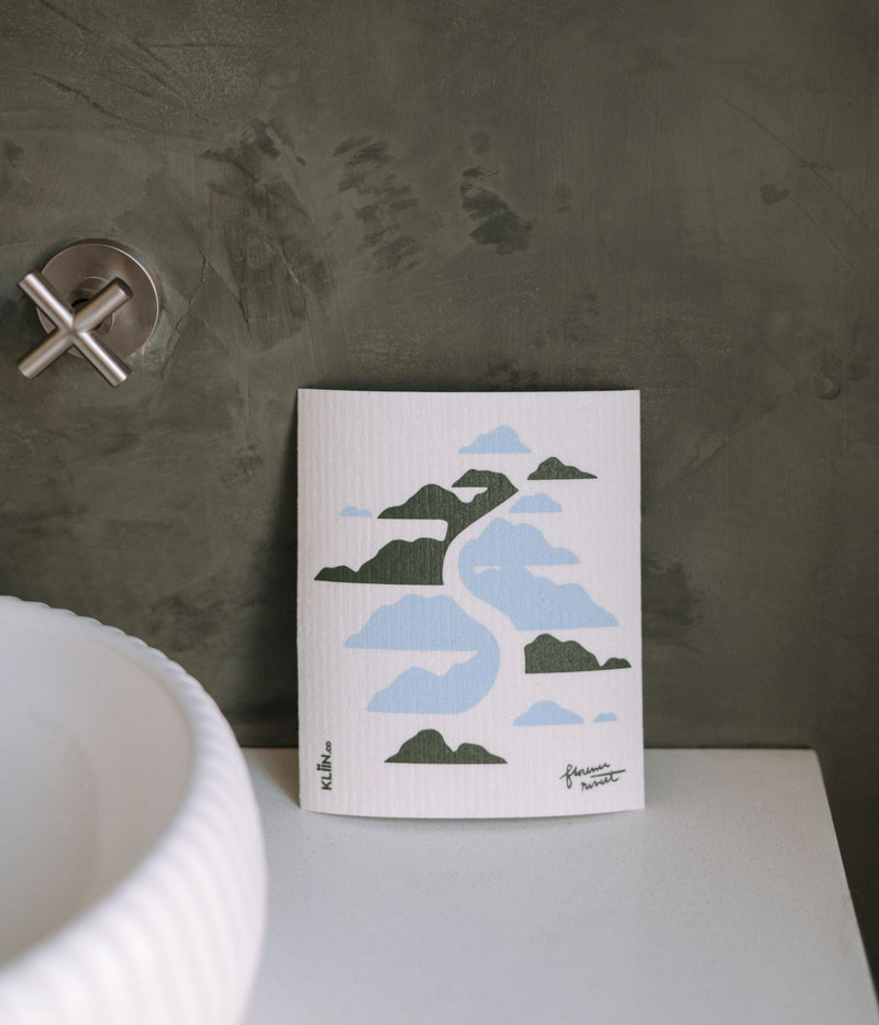 The TUC x Florence Rivest Kliin Reusable Cleaning Cloth | Valley placed on a bathroom counter, on the right of a sink.