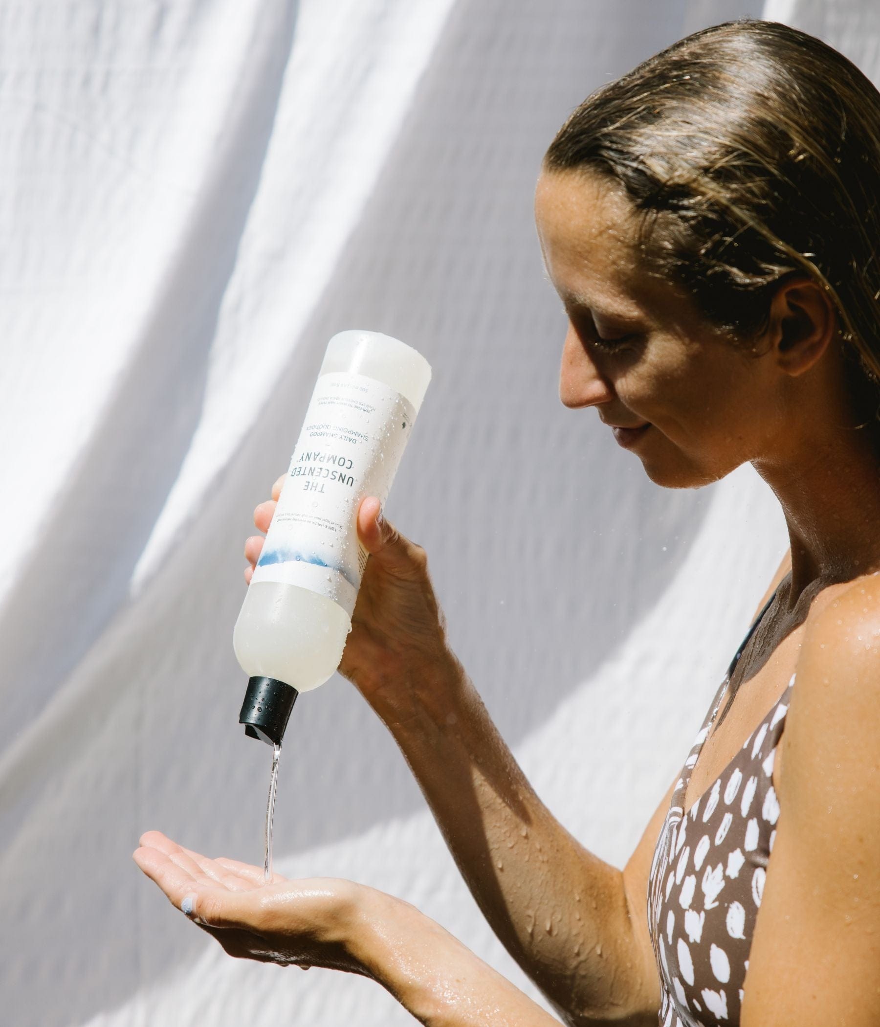 Woman applying The Unscented Company shampoo to her hand in the shower.
