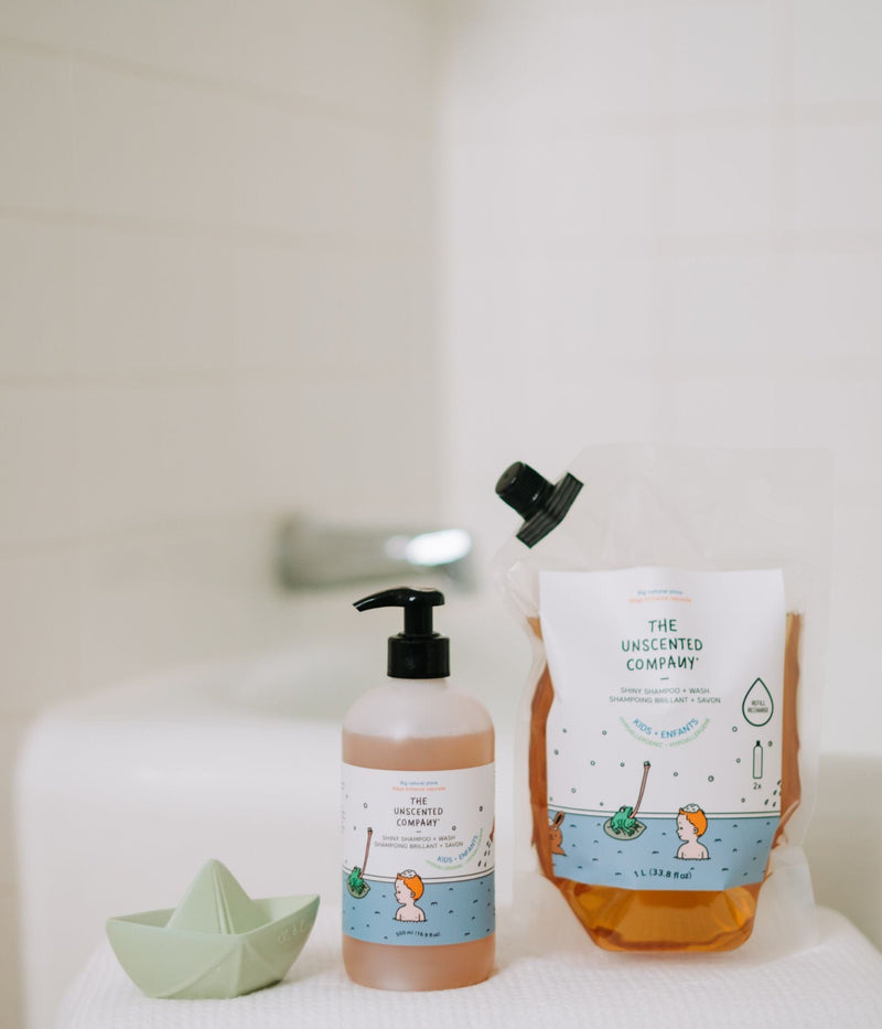 Kids shampoo bottle and refill pouch from The Unscented Company placed near a bath, with a green toy boat beside them.