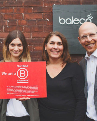 Three smiling people holding a Certified B Corporation sign in front of a Baleco sign.