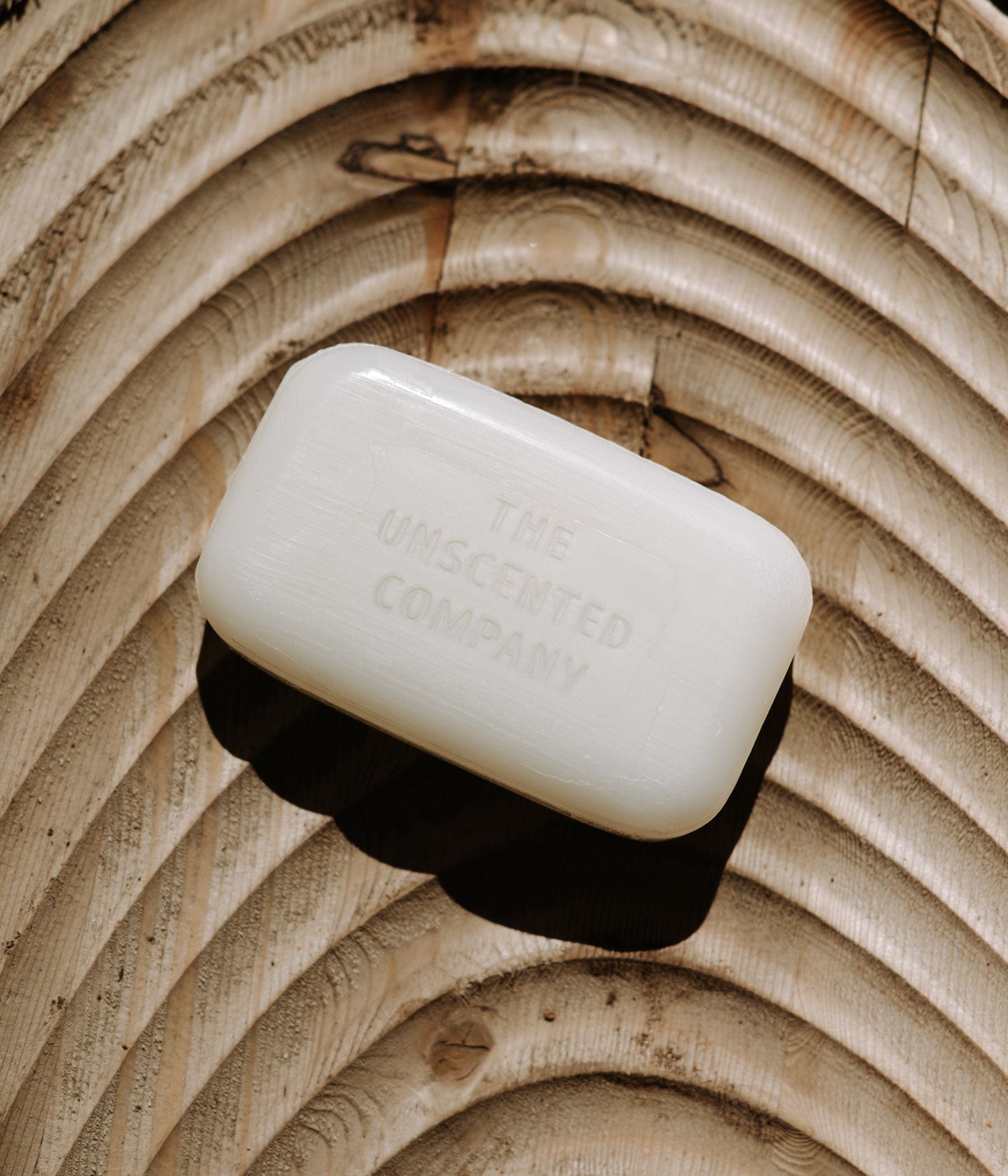 The Unscented Company soap bar resting on carved wood.