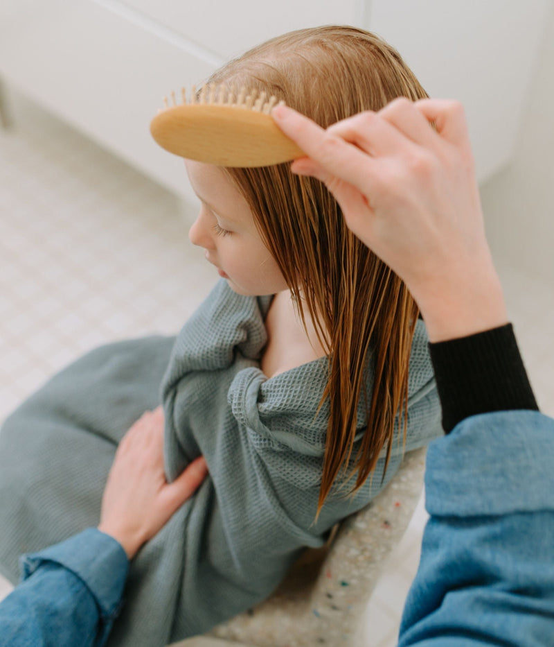 An adult brushes a child’s wet hair while the child sits wrapped in a towel.
