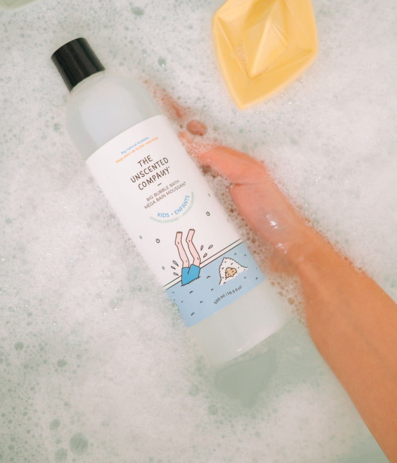 A hand holding a kids’ bubble bath bottle in a bubbly bathtub.