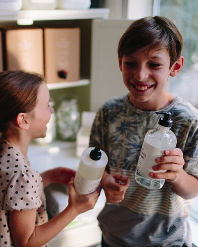 Two smiling kids holding bottles of soap