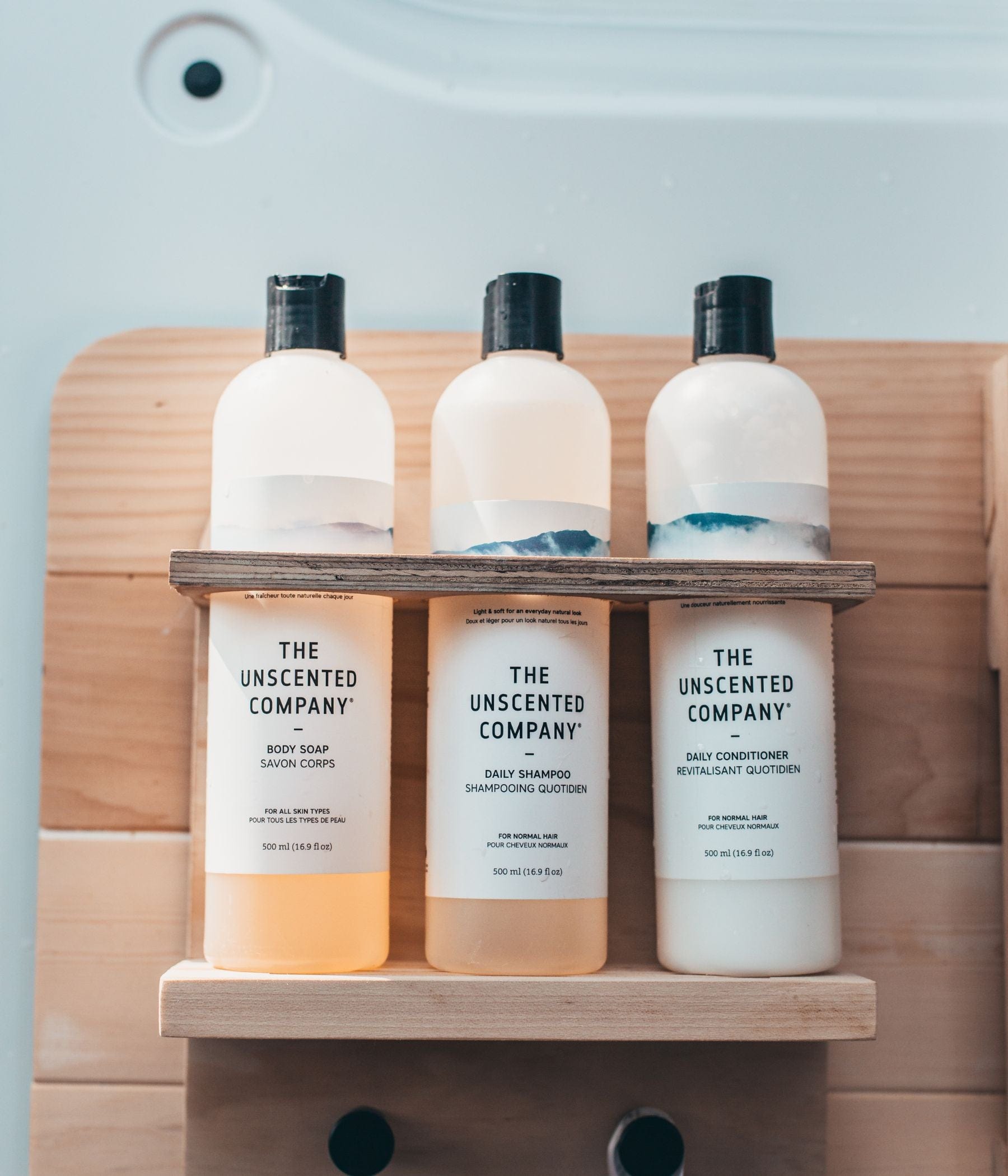 Three bottles of The Unscented Company products on a wooden shelf.