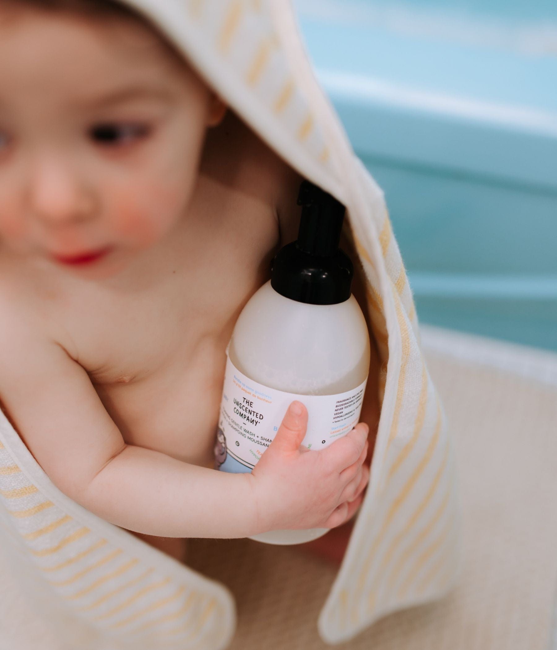 Baby wrapped in a towel holding a bottle of baby body wash.
