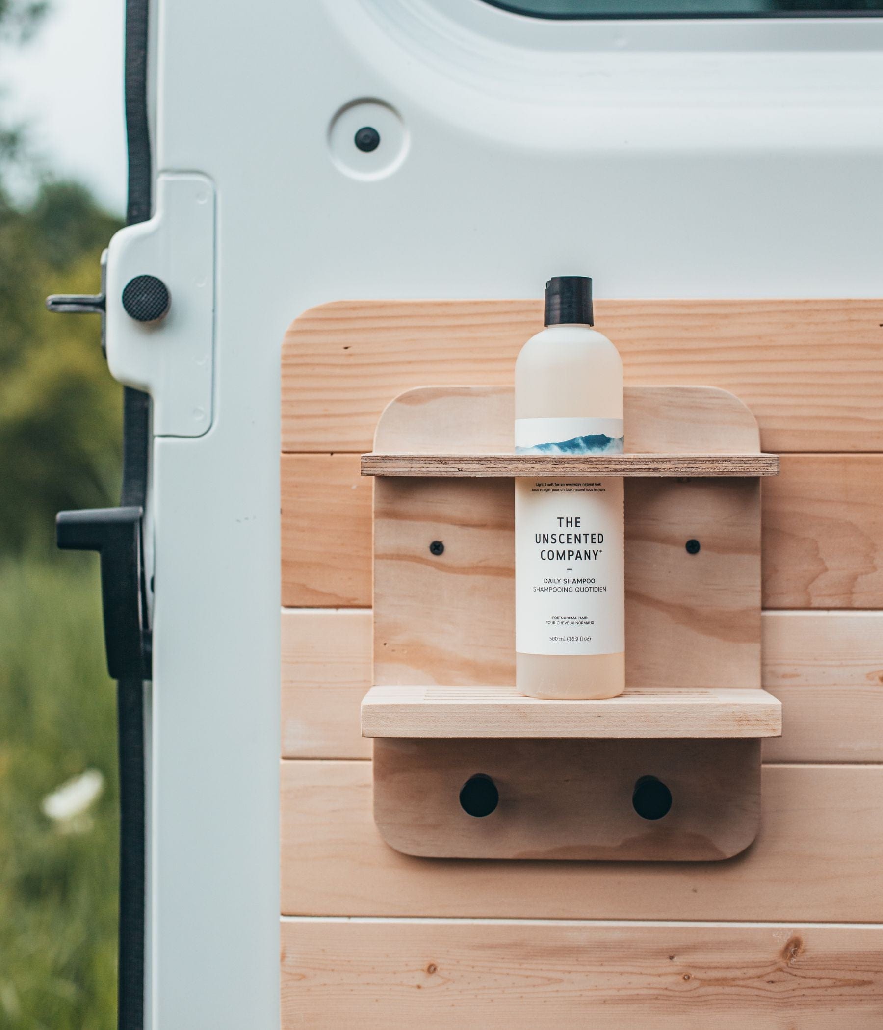 Shampoo bottle from The Unscented Company on a wooden shelf attached to a van door.