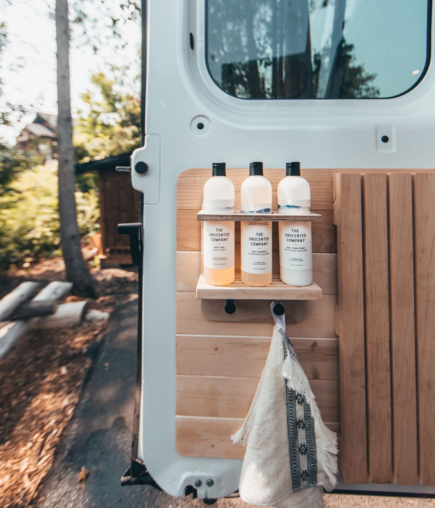Three bottles of The Unscented Company products on a wooden shelf inside a van door.