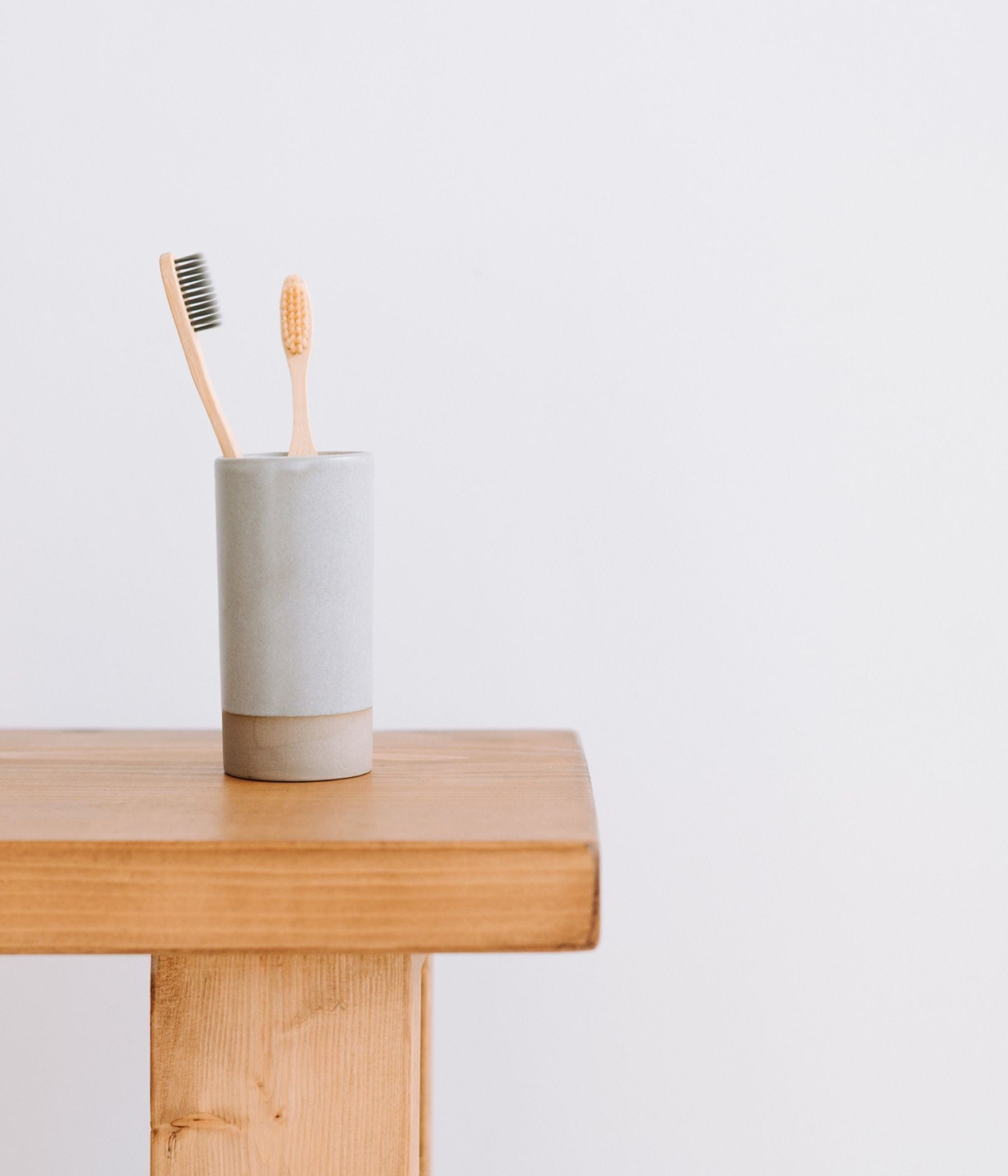 Two bamboo toothbrushes in a cup on a wooden surface.