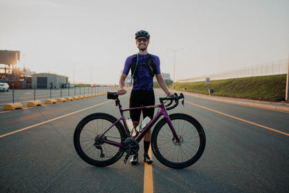 Cyclist standing on the road with a purple bike, smiling