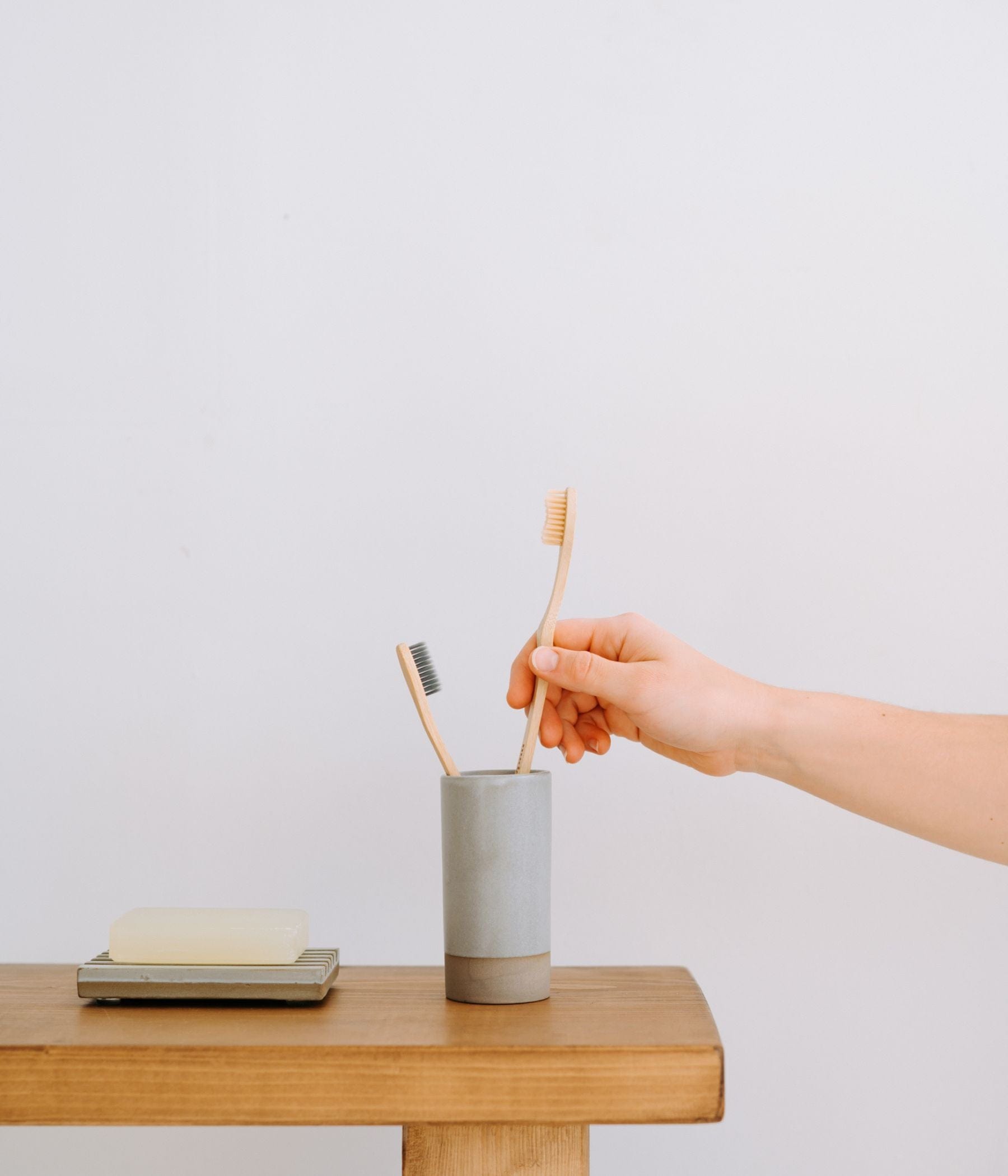 Hand picking a bamboo toothbrush from a cup next to a soap bar.