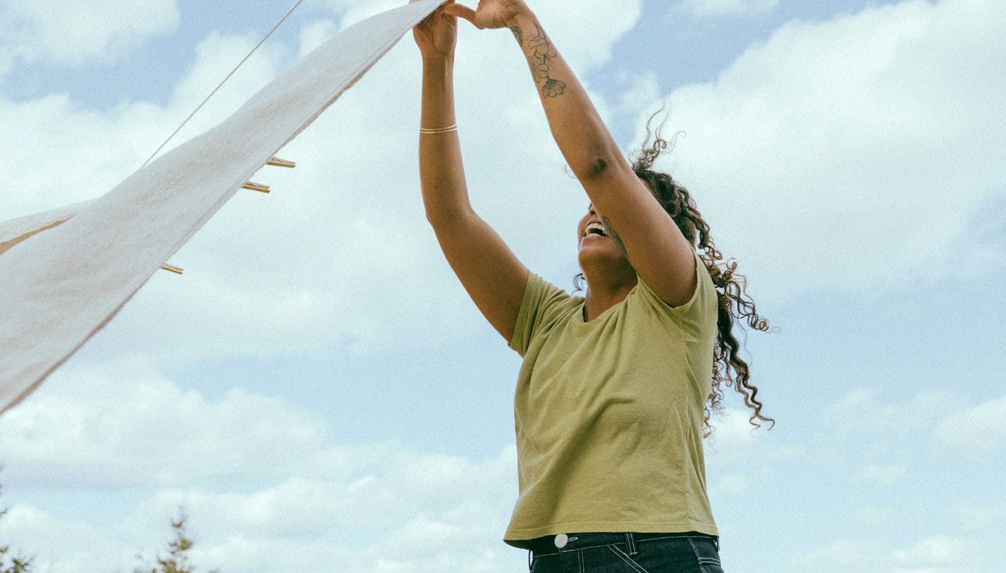 : Person hanging laundry on a clothesline under a blue sky.