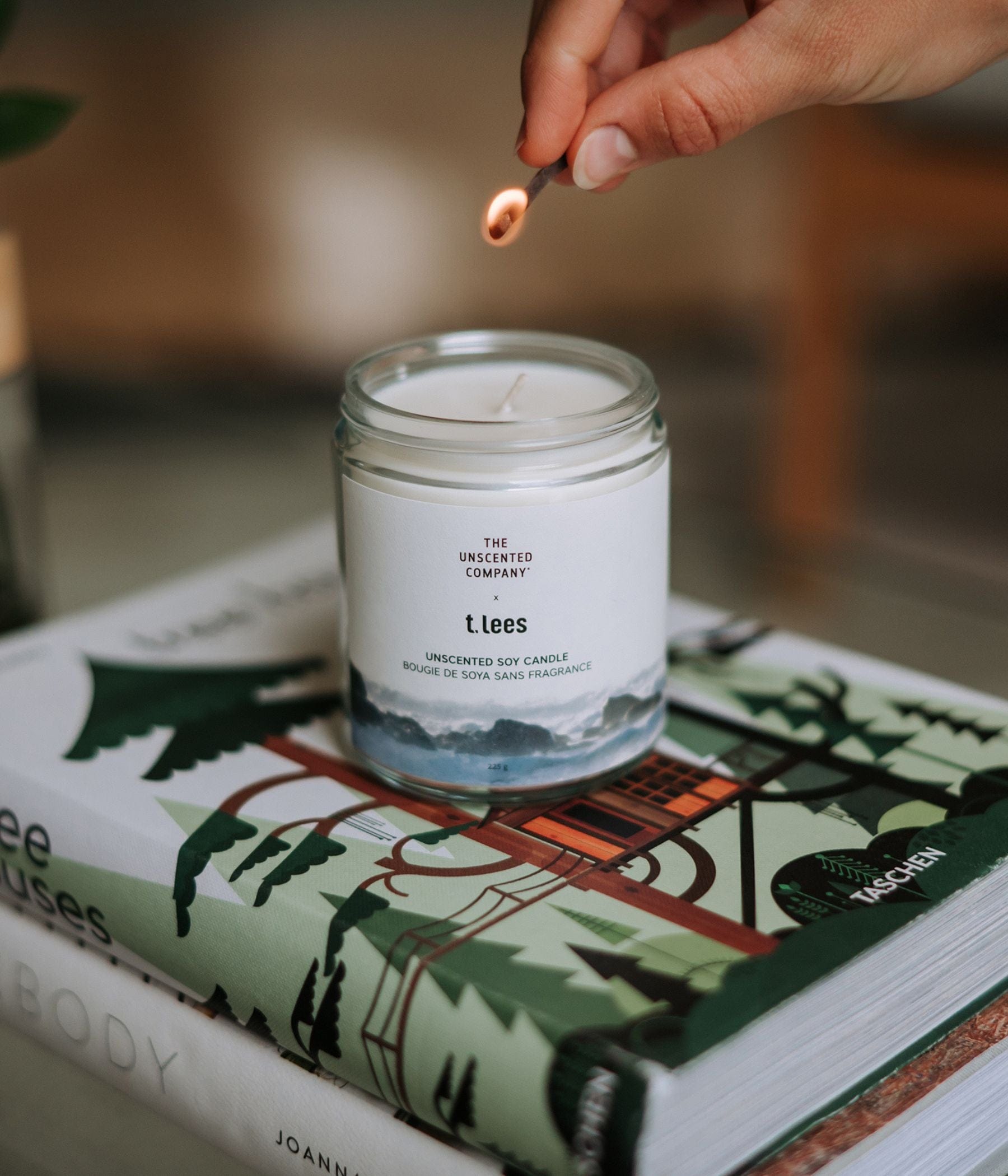A hand lights a candle by The Unscented Company on a book.