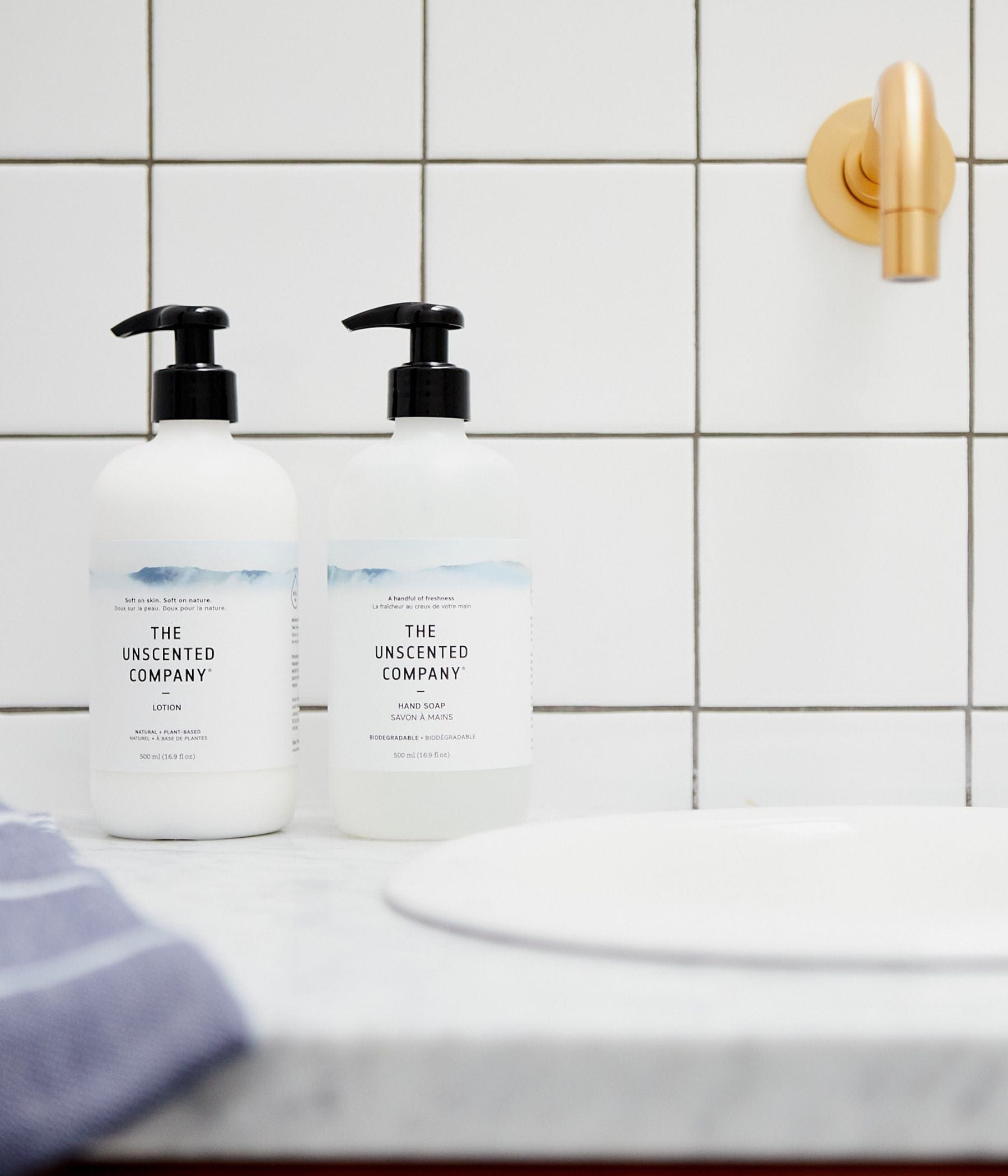 Two The Unscented Company bottles, lotion and hand soap, on a bathroom counter.