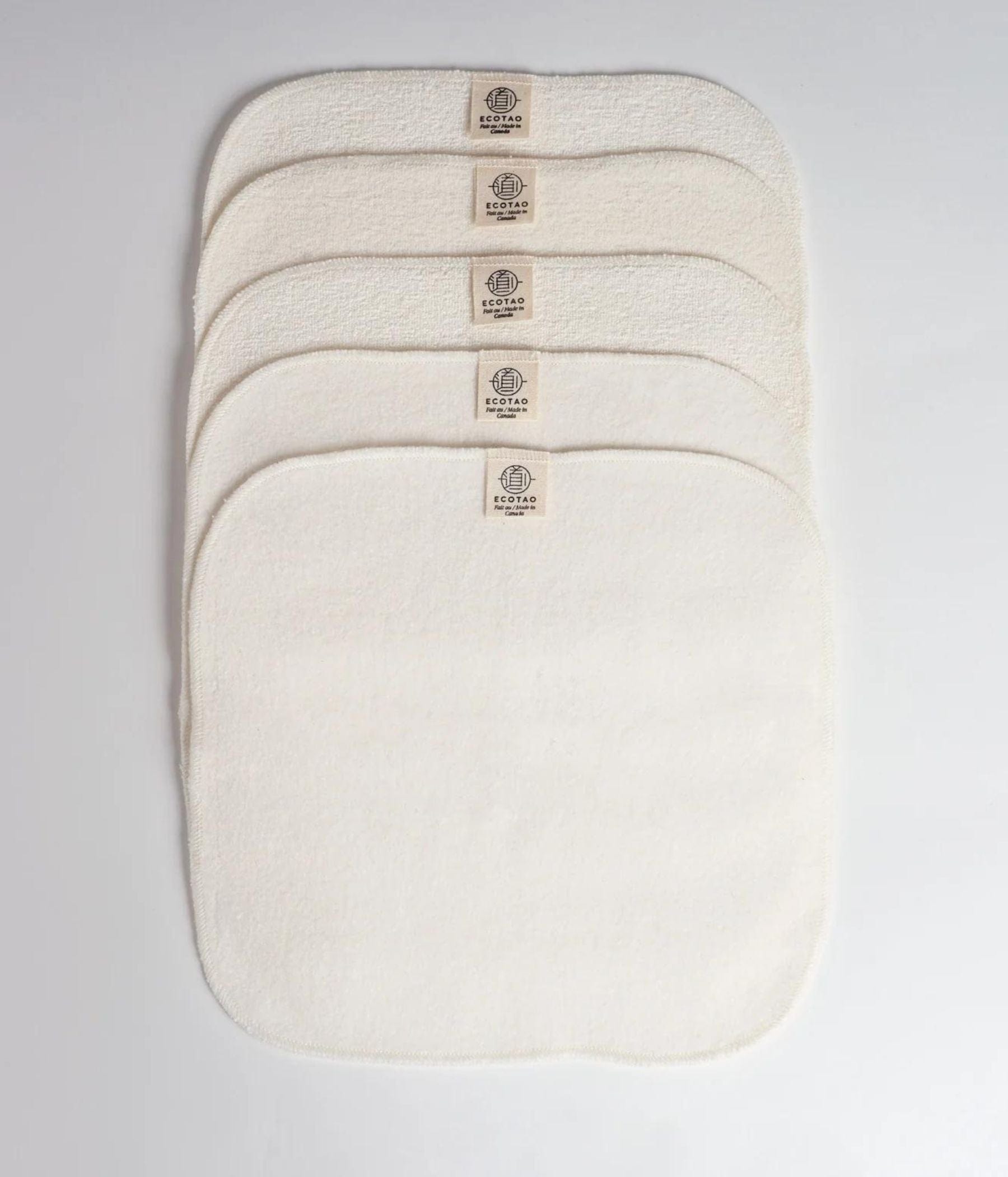 Ensemble de cinq linges réutilisables couleur crème empilés soigneusement sur un fond blanc.