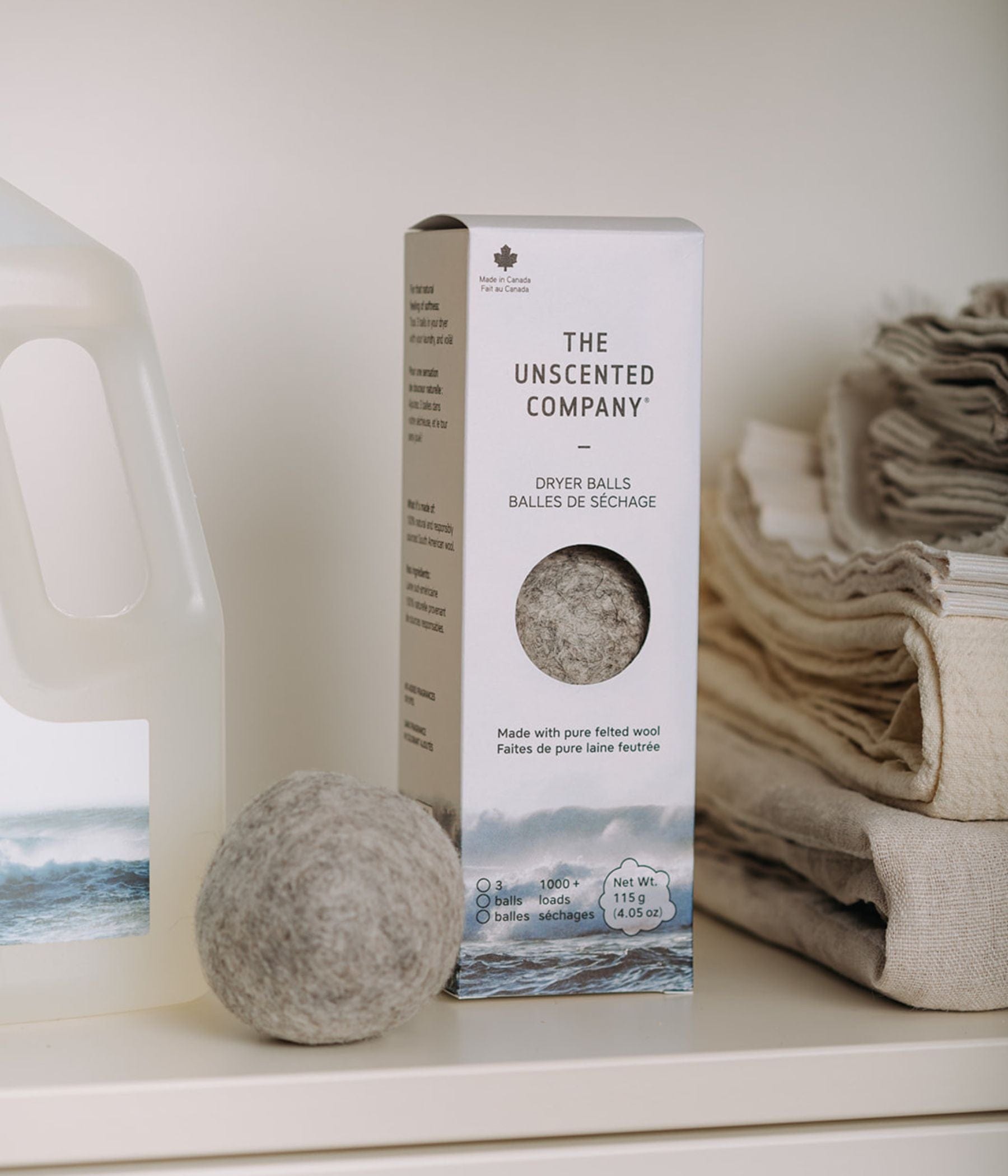 Box of The Unscented Company dryer balls with one wool ball in front, beside laundry detergent and folded linens on a shelf.