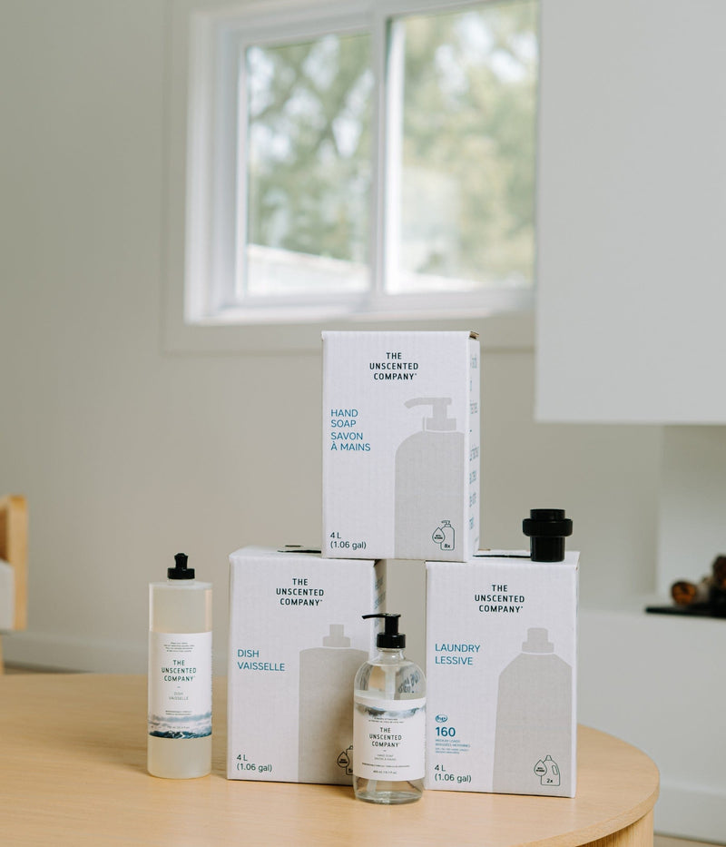 The Unscented Company At-Home Refill Station Kit featuring 4L bulk refills of laundry detergent, dish soap, hand soap, and all-purpose cleaner with reusable glass and plastic dispenser bottles on a white background.