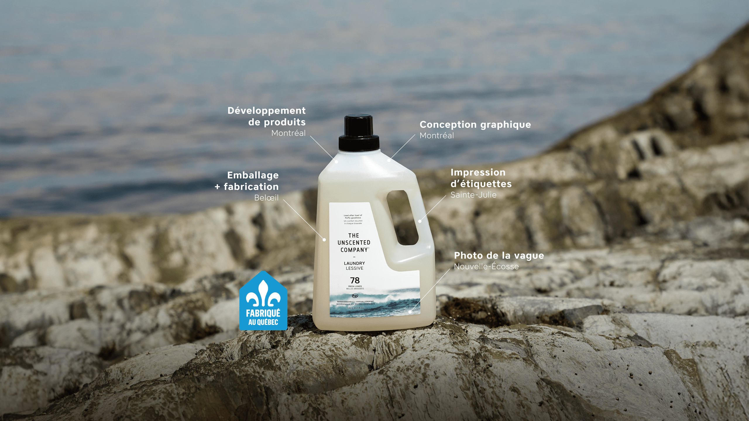Bottle of The Unscented Company laundry detergent on rocky shoreline with water in the background. Text points to production steps: product developed in Montréal, graphic design in Montréal, packaging and manufacturing in Beloeil, label printing in Sainte-Julie, and wave photo taken in Nova Scotia. A “Fabriqué au Québec” badge appears at the bottom left.