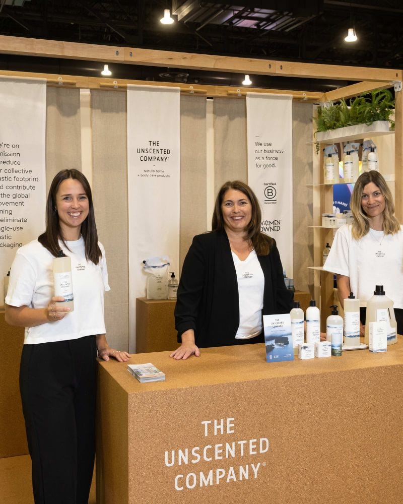 Three women at a booth with The Unscented Company products.