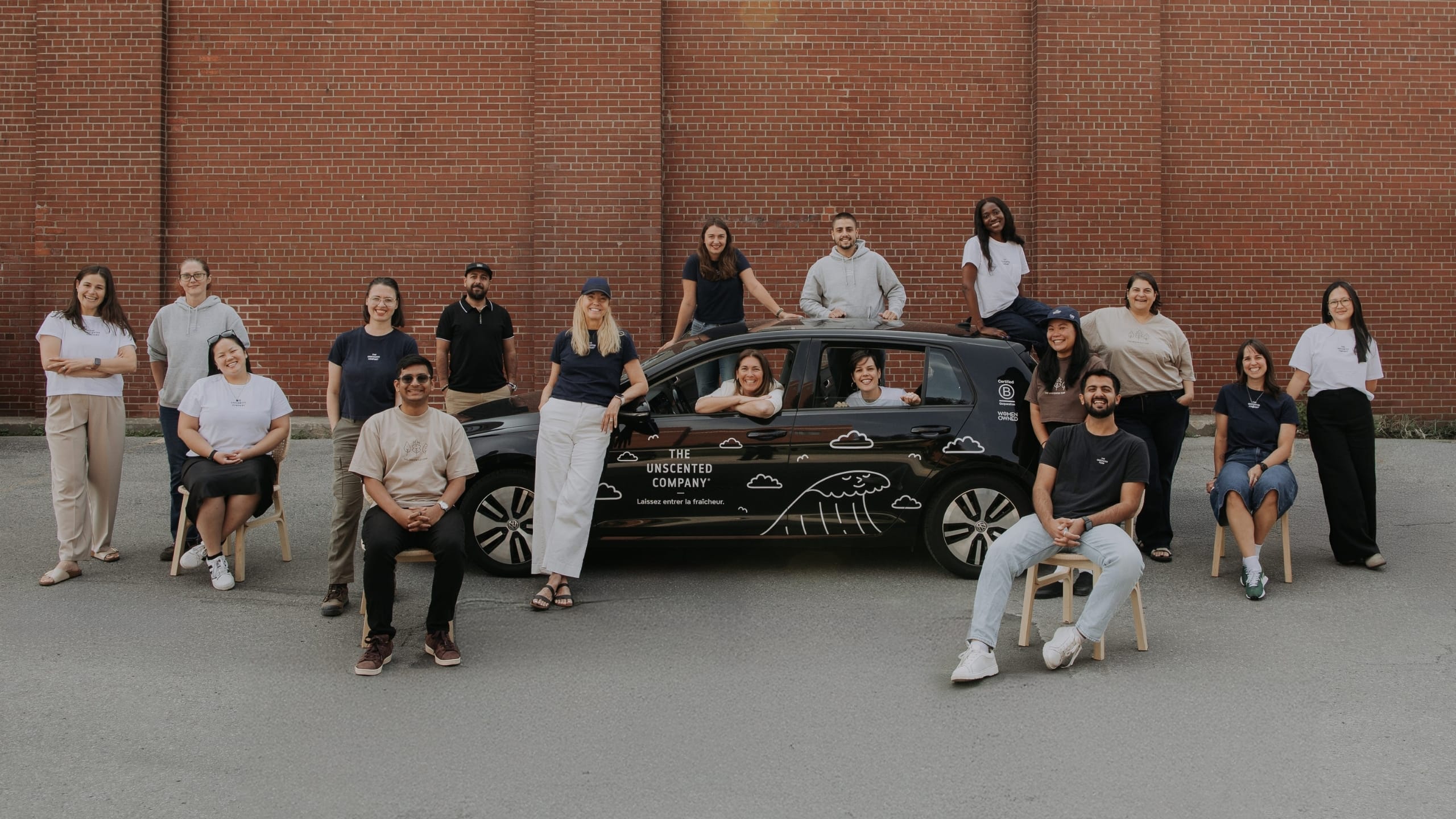 The Unscented Company team posing around their branded car, representing the sustainable Canadian home and body care company.