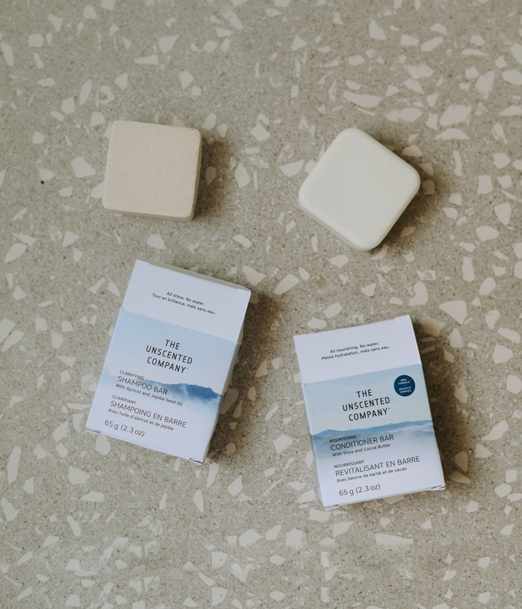 The Unscented Company solid shampoo and conditioner bars with their packaging, displayed on a terrazzo surface — fragrance-free and plastic-free hair care.