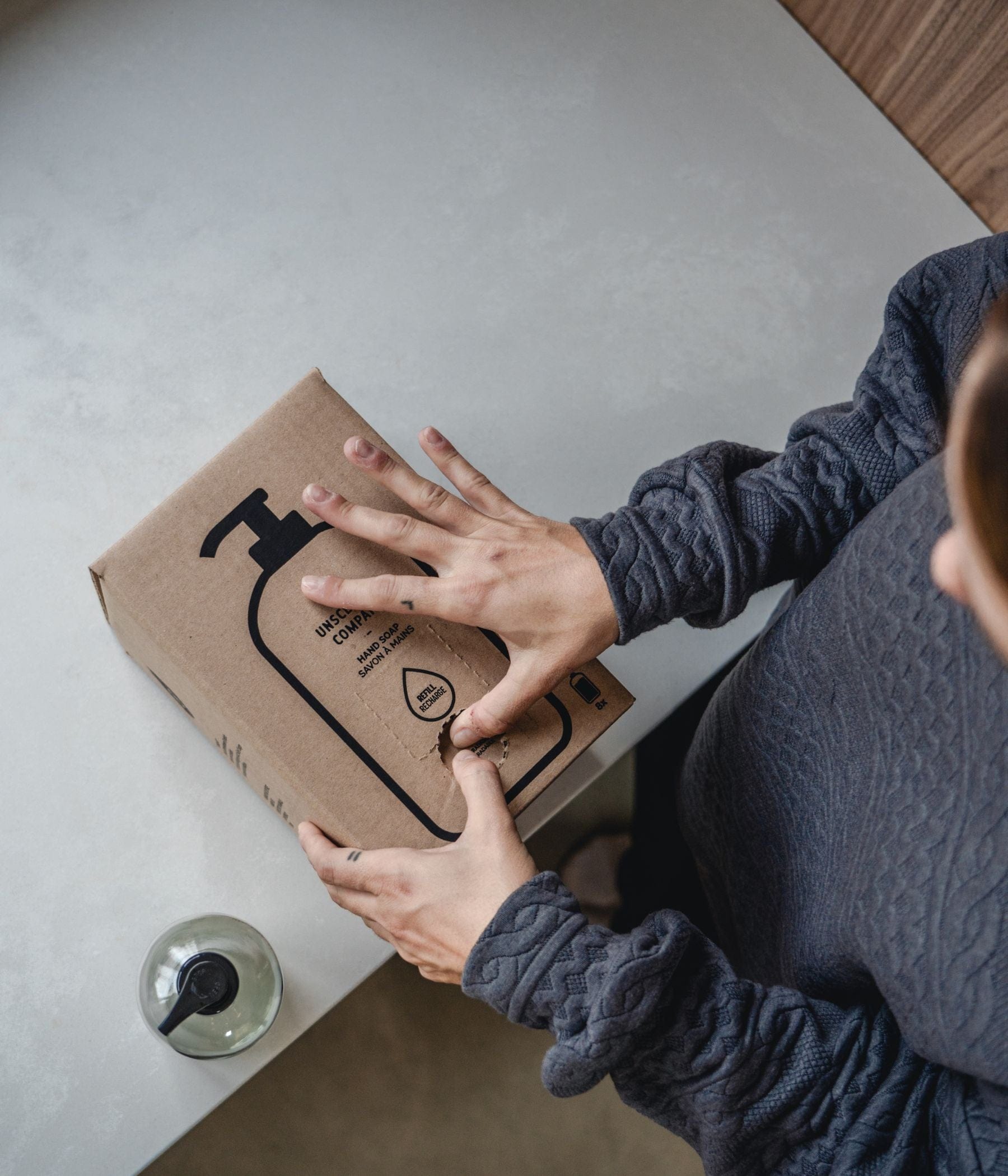 Person opening a cardboard box of The Unscented Company hand soap.