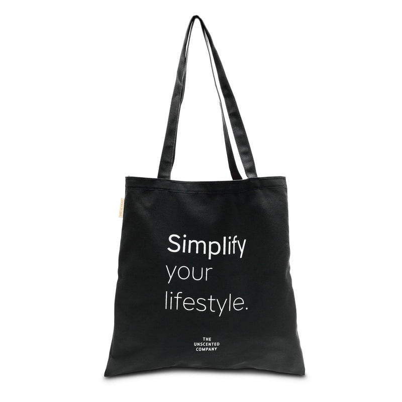 Black tote bag with long handles and white printed text that reads “Simplify your lifestyle.” with The Unscented Company logo underneath.