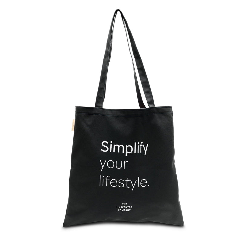 Black tote bag with long handles and white printed text that reads “Simplify your lifestyle.” with The Unscented Company logo underneath.