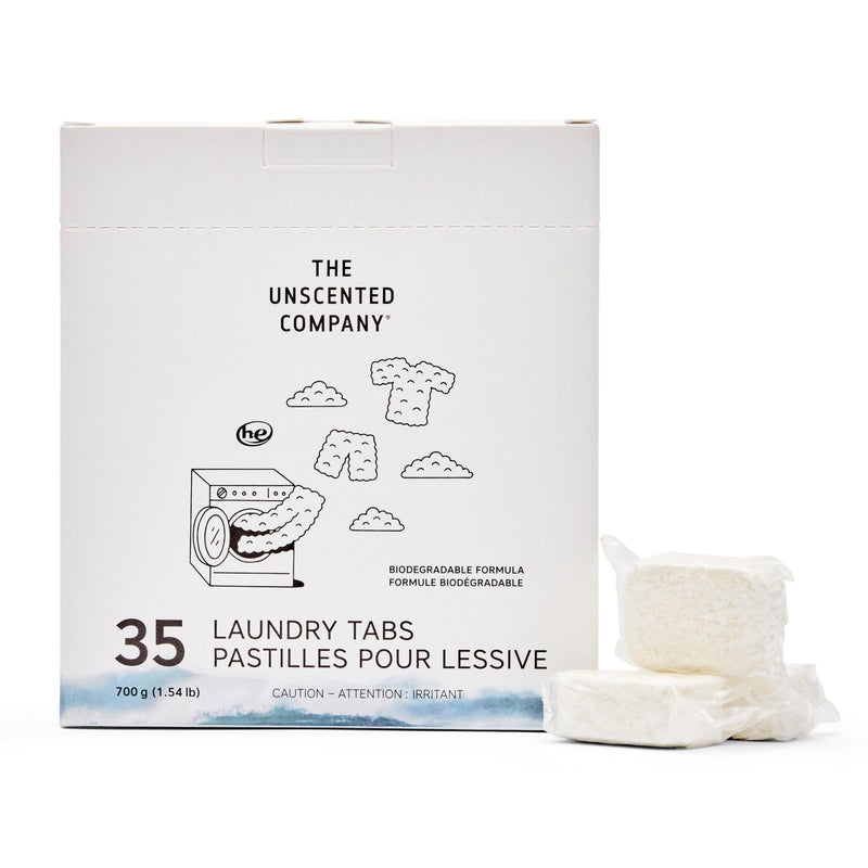Front of The Unscented Company laundry tabs box (35 count). Shows product name, weight, biodegradable formula claim, and illustration of a washer with floating clothes. Two unwrapped tabs placed beside the box.