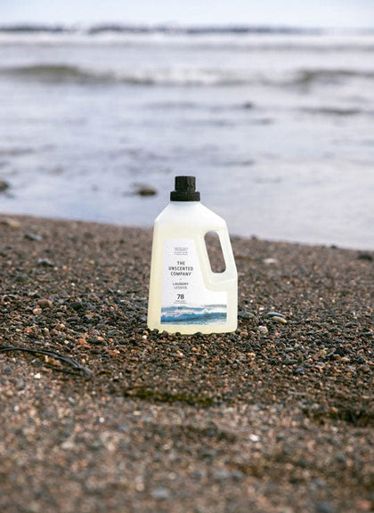 The Unscented Company laundry bottle on a rocky beach.